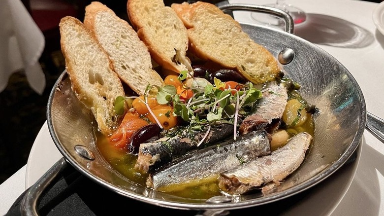 Sardines in a stainless steel bowl with a broth and crostinis