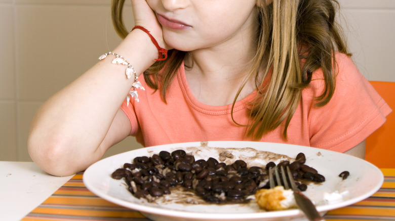 Annoyed little girl staring at plate of black beans