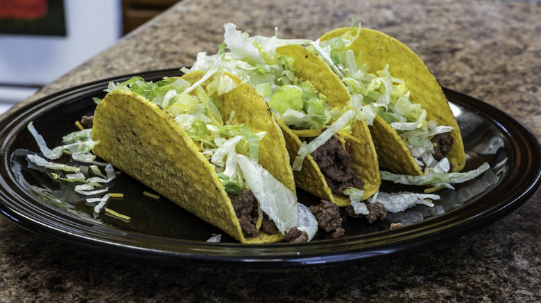 Crunchy shell tacos with ground beef on a black plate