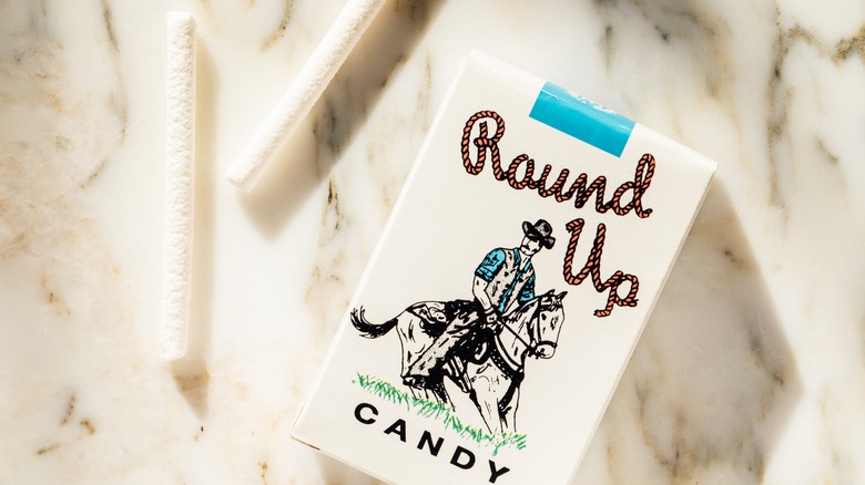 Box of candy cigarettes on marble surface with two candies sitting outside package