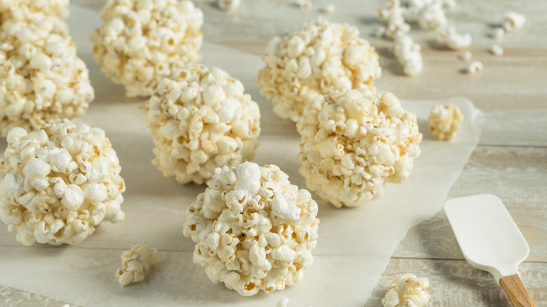 Homemade popcorn balls lined up on wax paper with stray popcorn pieces and a spatula nearby