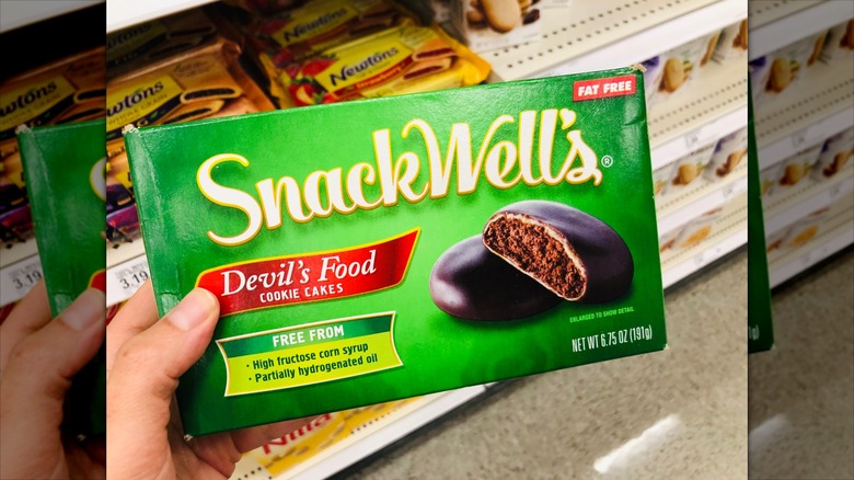 Hand holds a package of Snack Wells brand devils food cookie cakes. This is a fat free food, and diet friendly dessert.