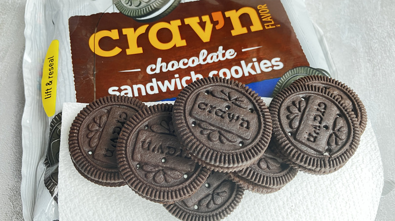 Crav'n chocolate sandwich cookies engraved with the brand name, lined up along the edge of a package of cookies.