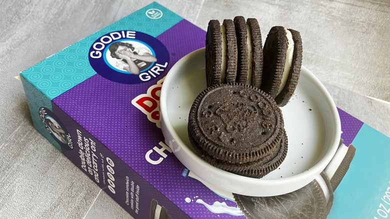 Goodie Girl chocolate sandwich cookies fill a small white dish sitting on top of a blue and purple box of cookies.