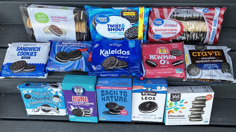 Thirteen packages of chocolate sandwich cookies from different labels lined up in three rows, incuding brands like Trader Joe's, Great Value, and Amazon