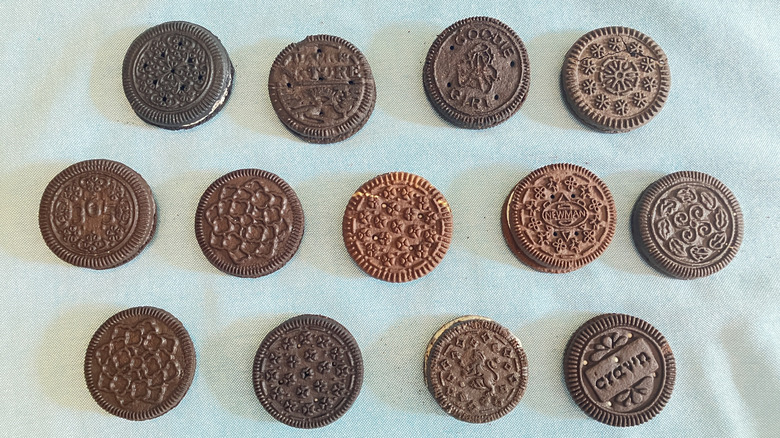 Top view of thirteen Oreo cookie dupes of various colors and patterns lined up in three rows, including brands like Crav'n, Goodie Girl, and Newman