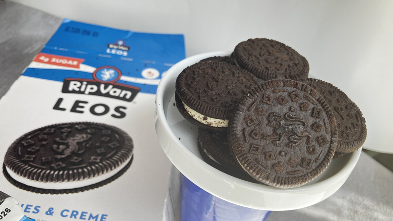 A close up shot of Rip Van Leos chocolate sandwich cookies piled in a small white dish with a blue and white cookie box in the background.