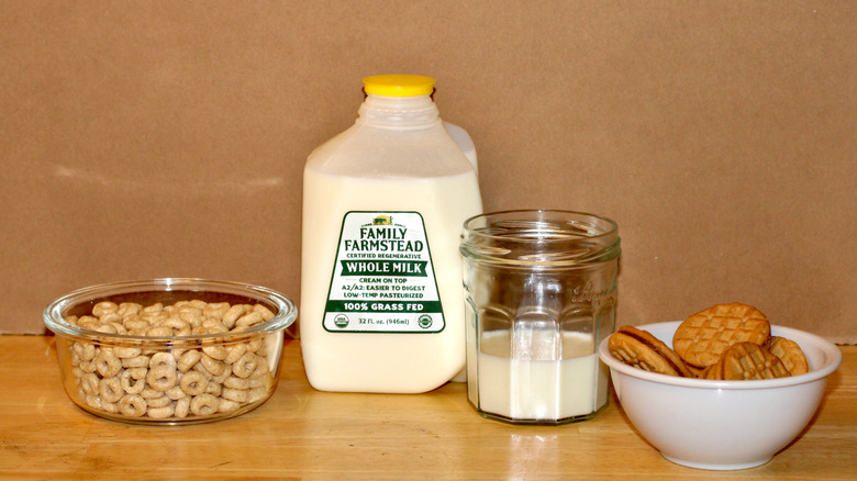 A Family Farmstead brand carton of non-homogenized grass fed organic whole milk beside a glass of milk, a bowl of cereal, and some cookies