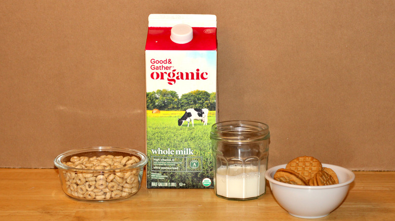 A Good & Gather brand carton of organic whole milk beside a glass of milk, a bowl of cereal, and some cookies