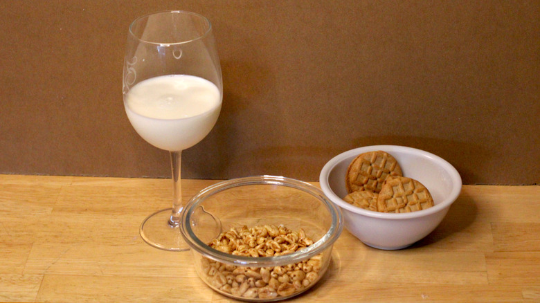 A glass of whole milk beside a bowl of cereal and some cookies