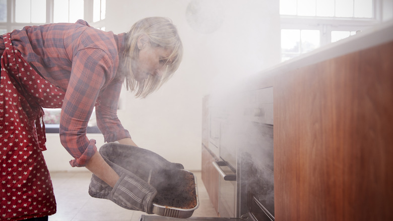 Woman taking food out of smoke filled oven