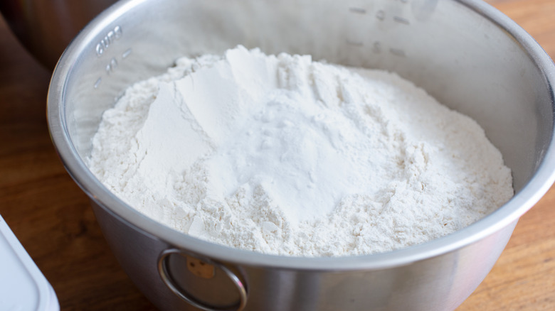 A steel bowl of all purpose flour on a wooden table