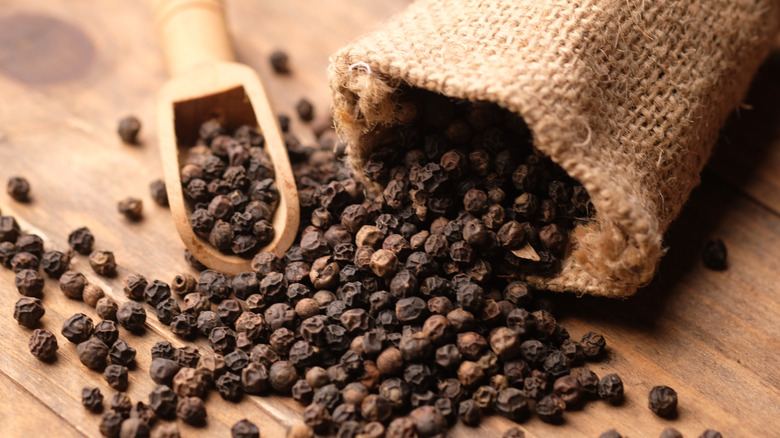 Black peppercorns in a burlap bag and a wooden spoon