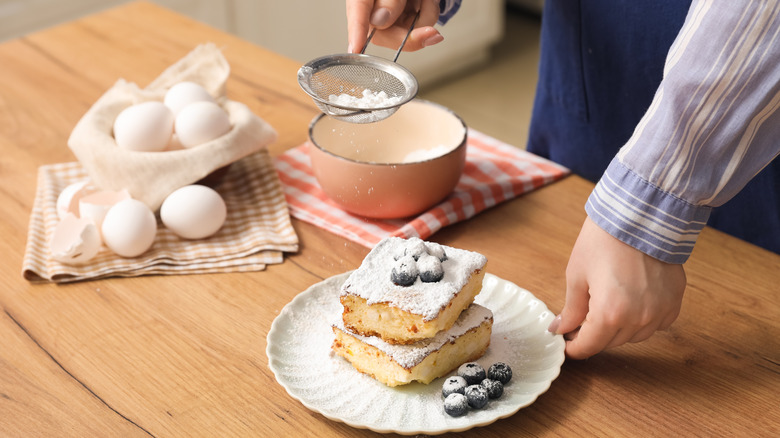 A pastry chef's hands sprinkling confectioners sugar over a piece of cake