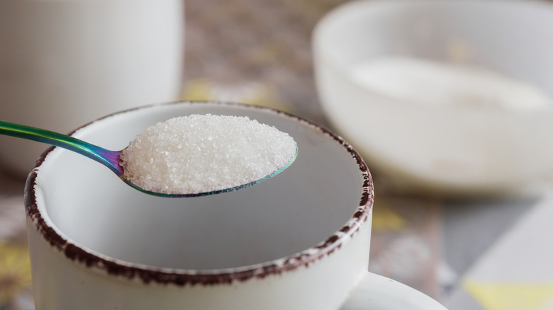 A spoon of granulated sugar over a coffee cup
