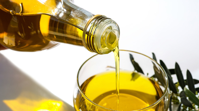 Olive oil pouring from a bottle into a glass bowl