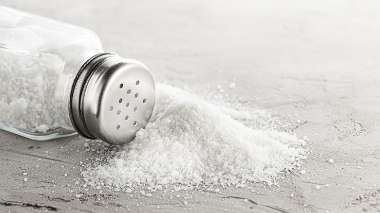 A salt shaker tipped on its side with a pile of salt in from of it