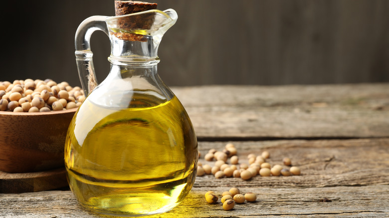 A glass jug of vegetable oil on a wooden table in front of a bowl of soy beans