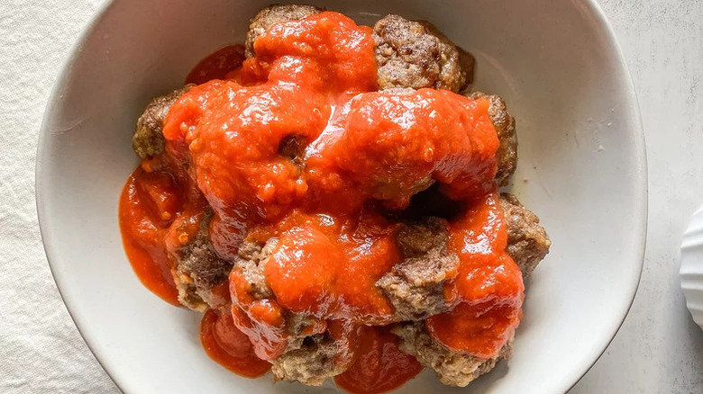Meatballs covered in marinara in a white bowl