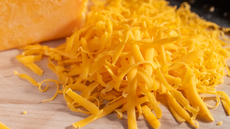 A block of cheese and shredded cheese on a wooden board