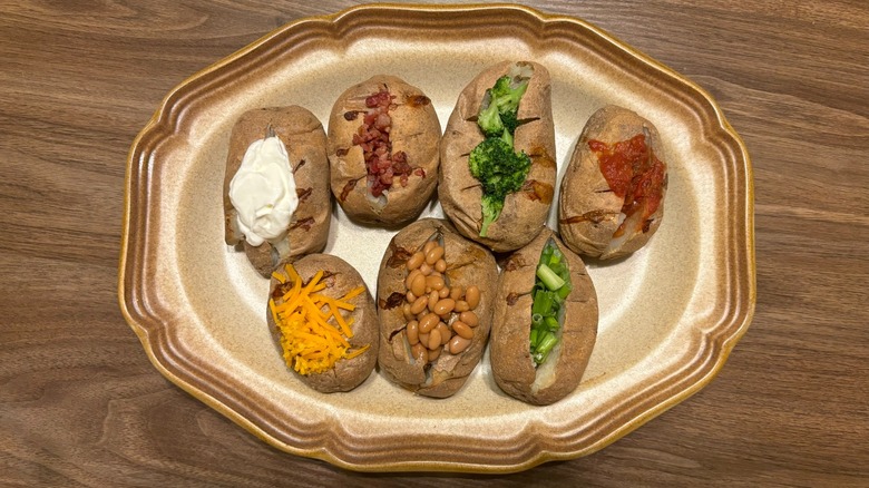 many baked potatoes with various toppings on a platter, including toppings like salsa, broccoli, and baked beans