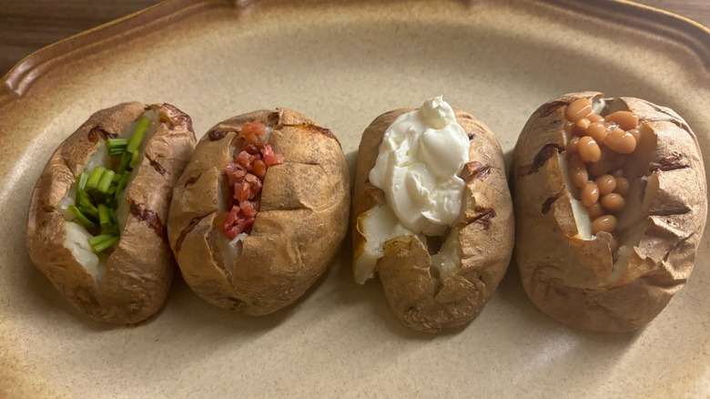 a few baked potatoes with various toppings on a platter, including toppings like sour cream, bacon bits, and chives