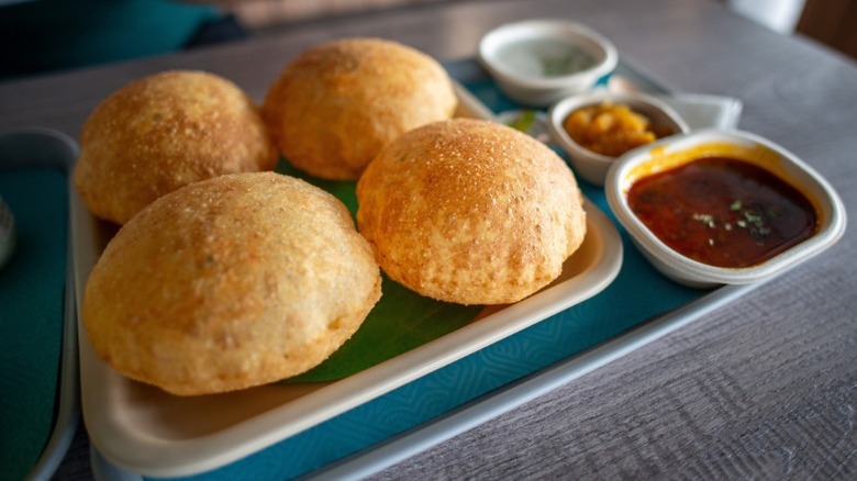 tTay with four puri with sides of potato and other chutneys