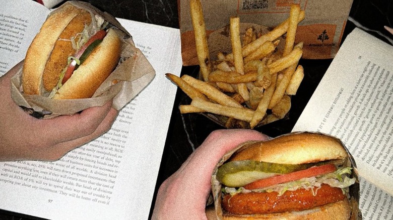 Hands holding chicken sandwiches from Harvey's with a side of fries above two open books