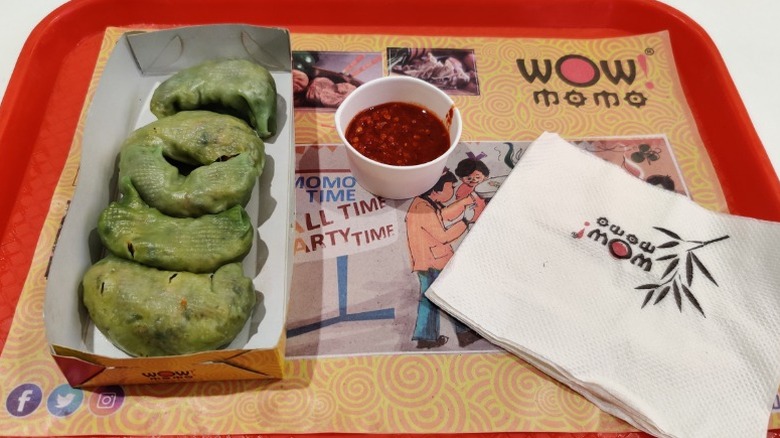 Tray of food from Wow! Momo restaurant chain, including green-colored dumplings and a cup of red sauce