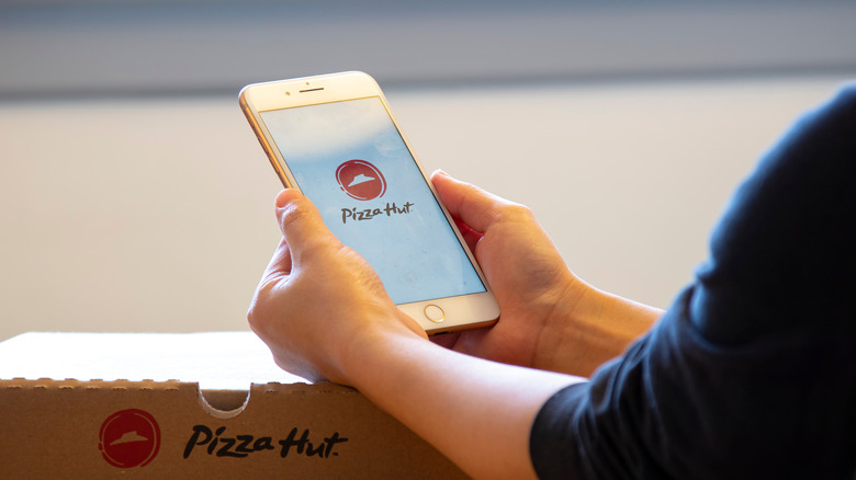 Someone holding an iPhone showing the Pizza Hut app