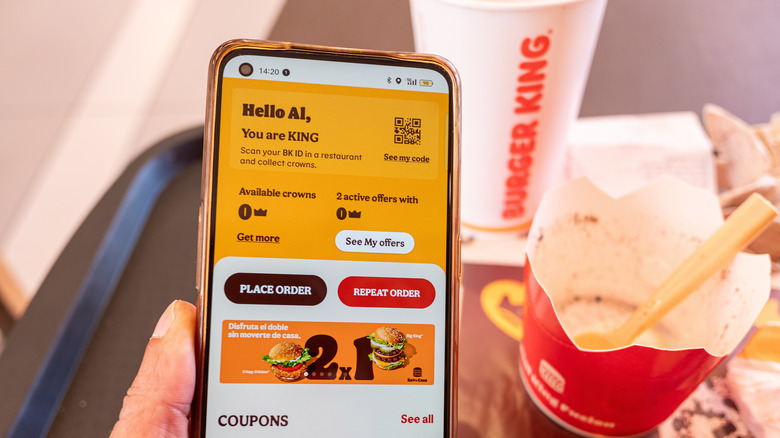 Someone sitting in front of a full Burger King tray holding phone that's displaying the Burger King app