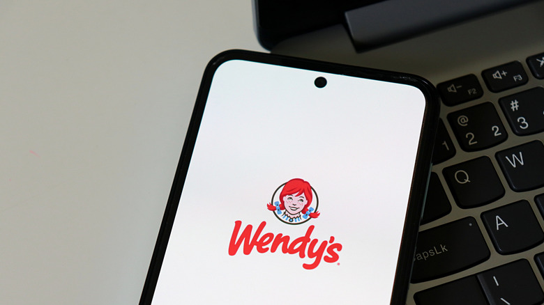 A phone displaying the Wendy's logo resting on a laptop.