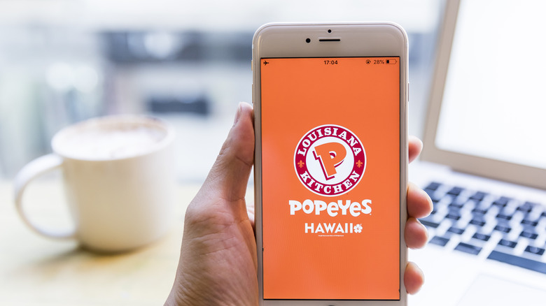 A hand holding a phone that has the Popeyes app open.
