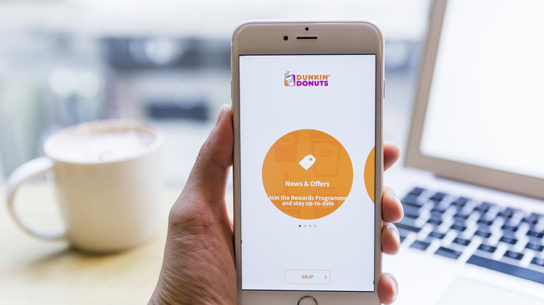 A hand holding a phone displaying the Dunkin' app