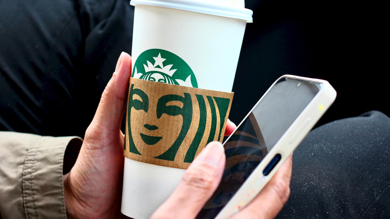 Someone holding a Starbucks cup and a white phone.