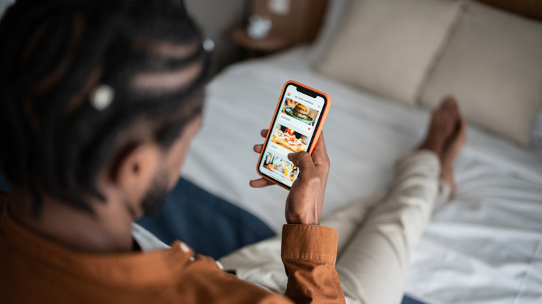 A man sitting in bed, reviewing a food app.