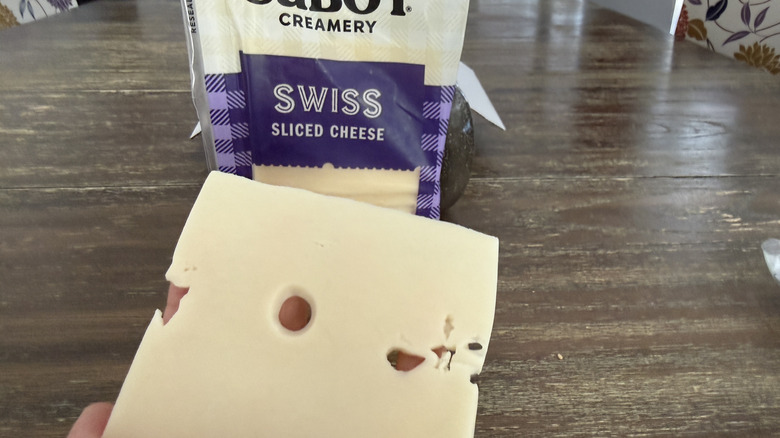 Hand holding a slice of Cabot Swiss cheese