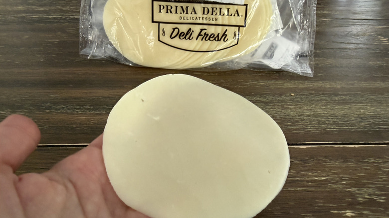 Hand holding a slice of Prima Della Sliced Provolone