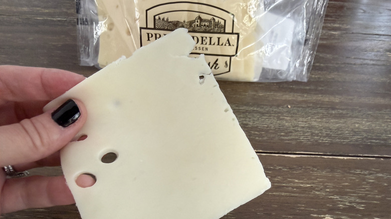 Hand holding a slice of Prima Della Swiss cheese