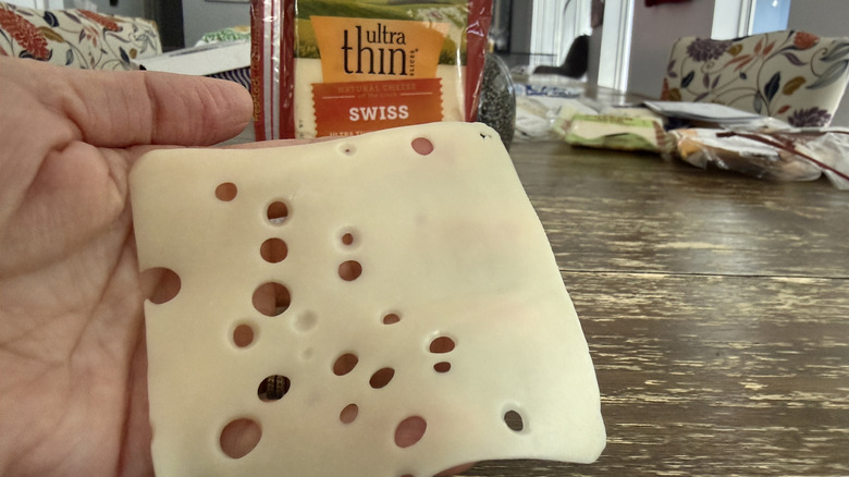 Hand holding a slice of Sargento ultra thin Swiss cheese