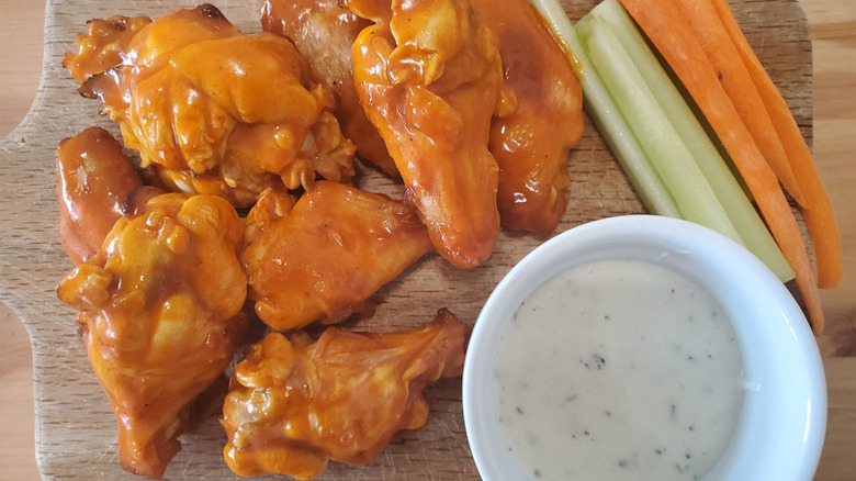 Buffalo chicken wings on a wood serving board with celery, carrot sticks, and a ramekin of ranch dressing