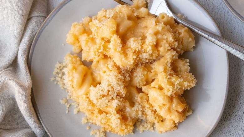 Homemade mac and cheese shot overhead on a white plate with a fork and linen napkin