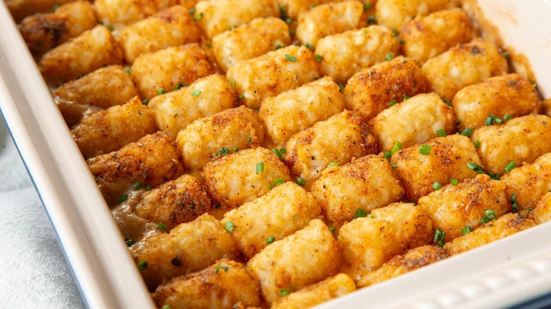 A white baking dish of homemade cowboy casserole topped with tater tots and fresh chives