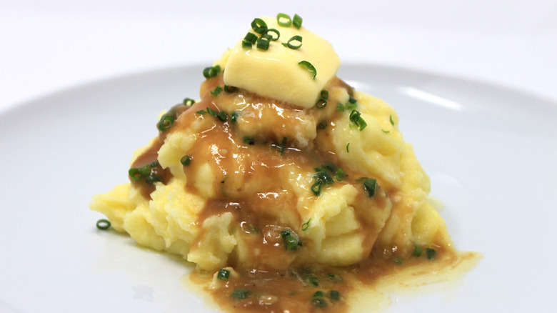 A single serving of millionaire mashed potatoes topped with gravy, a pat of butter, and fresh chives on a white plate