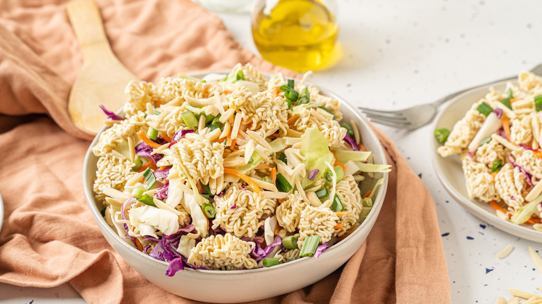 Ramen noodle salad in a white serving bowl styled with a linen cloth and a glass bottle of dressing