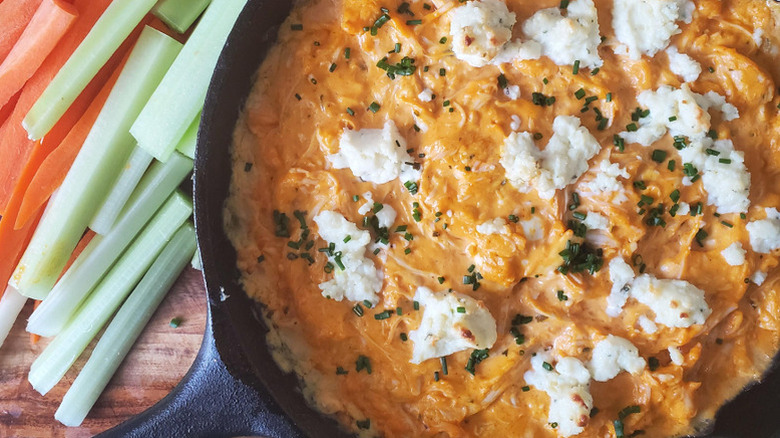 Buffalo chicken dip in a cast iron skillet next to fresh celery and carrot sticks