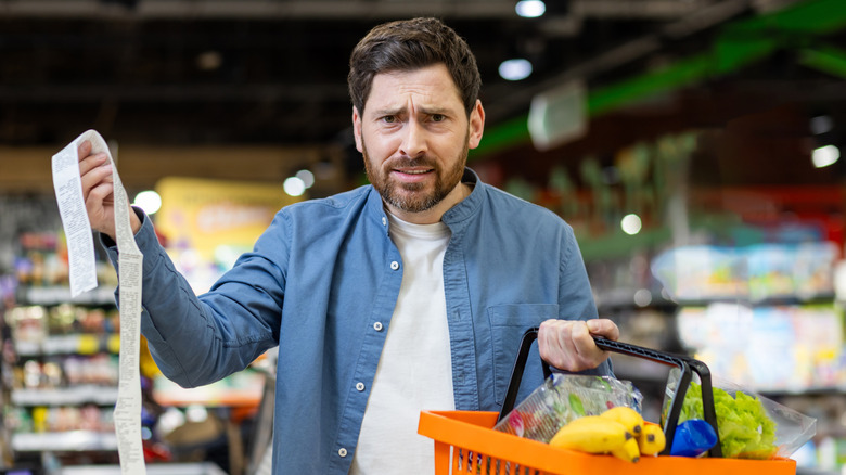 A shopper at a supermarket upset while holding a receipt.