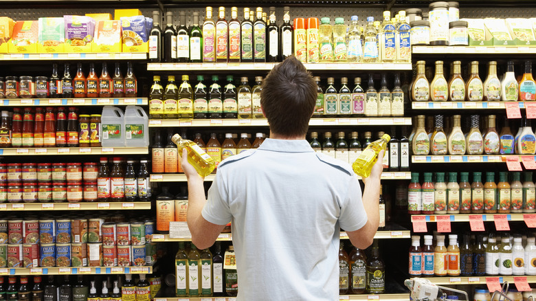 A man looking at supermarket shelves while holding bottles in his hand