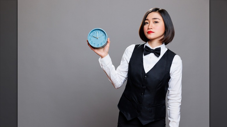 server holding clock with disappointed look on her face