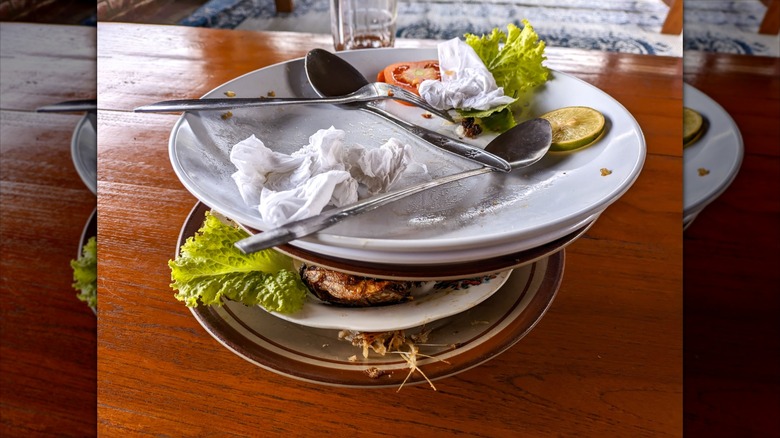 A stack of dirty plates with leftover food and spoons
